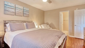Quarto com cama, ventilador de teto e três quadros na parede.