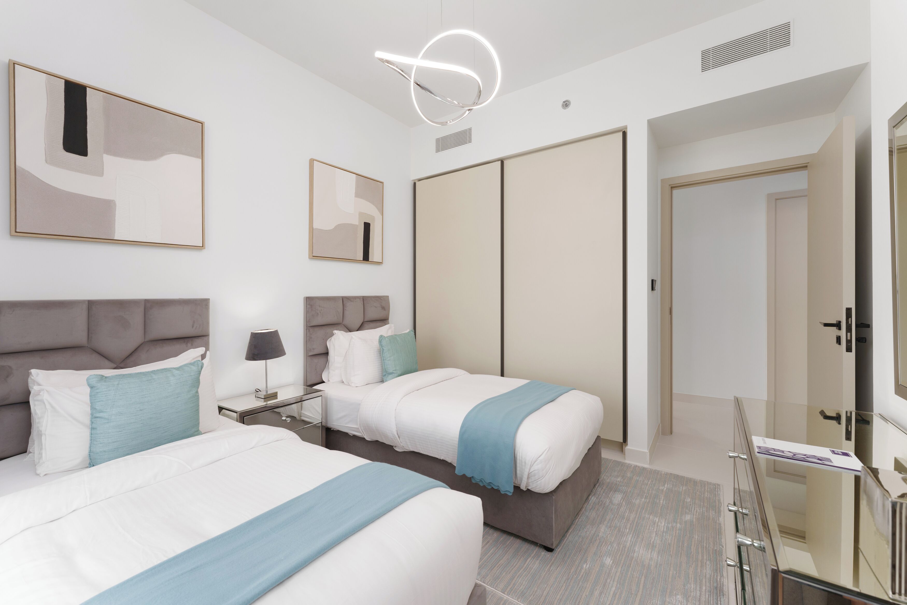 Une chambre d’h ôtel moderne avec deux lits, une table de chevet avec une lampe, un grand miroir et une armoire.