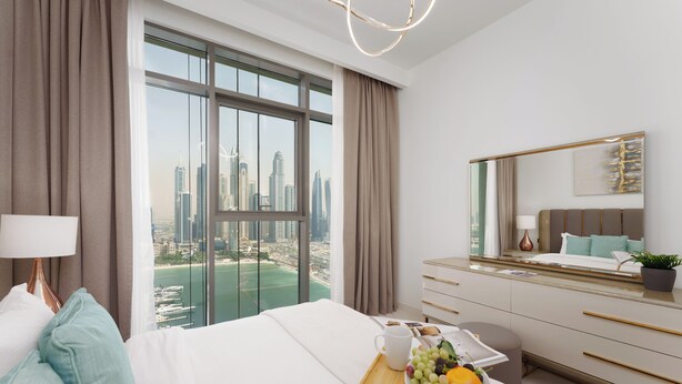 Ein modernes Hotelzimmer mit großem Fenster und Blick auf die Stadt, einem ordentlich bezogenen Bett, einem Nachttisch mit Obstschale und einer schlichten Kommode.