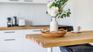 A kitchen counter with a white vase containing white flowers and green leaves, a wicker basket, and a white cup on a saucer. - Résidence Paris SEVRES (Paris)