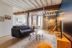Un soggiorno moderno con un divano scuro, un tavolino rotondo e un tappeto decorato. Si distingue un'area pranzo con tavolo e sedie, e sullo sfondo si vede una cucina.