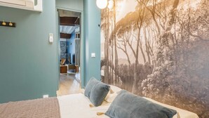 A bedroom with a bed, pillows, a wall mural, and a hallway leading to another room. - Résidence Paris SEVRES (Paris)