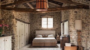 A rustic bedroom with a stone wall, wooden beams, a large bed, a window, a bedside table, and a lamp. - Le Porciglia by Boutique (Colle di Val d'Elsa)