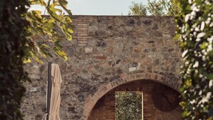 An outdoor seating area with stone walls, a table, and a window with a view of greenery. - Le Porciglia by Boutique (Colle di Val d'Elsa)