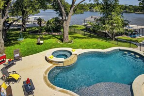 A swimming pool with a hot tub, surrounded by a deck with lounge chairs and a view of a lake. - Bluebonnet Retreat Haven | Concierge Services (Kingsland)