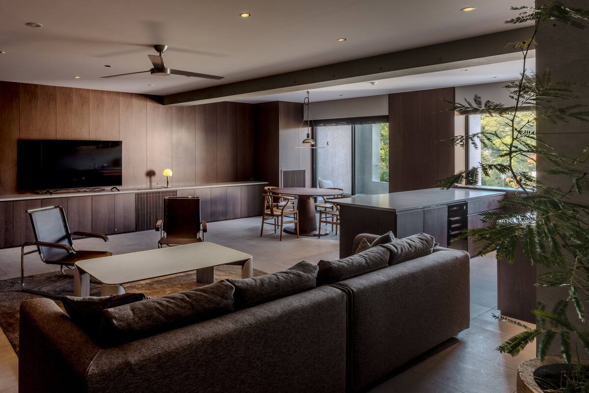 Un salon moderne avec un canapé, une table basse et un téléviseur. On y trouve également un coin repas avec des chaises et une table, ainsi qu'une cuisine dotée d'une grande fenêtre.