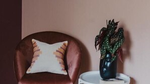 Una habitación con un sillón de cuero marrón, un almohadón blanco, una mesita de noche pequeña blanca y un cuadro en la pared.