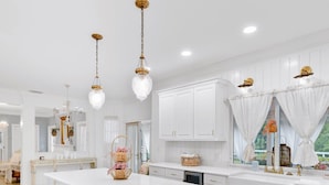 Una cocina amplia con una isla grande, armarios blancos e iluminación colgante.