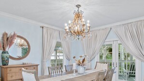 Comedor con una mesa de madera, sillas, un candelabro y vistas al exterior con vegetación.