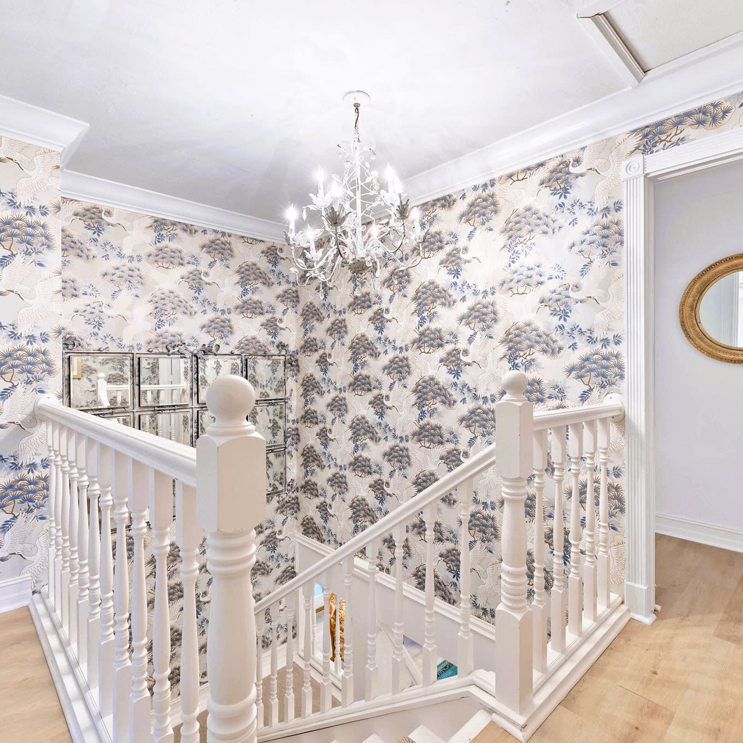 Een trap met witte balustrades en een behang patroon met bloemen.