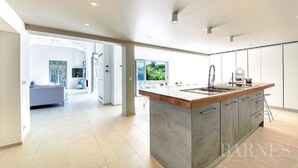 A modern kitchen with a central island, large windows, and a view of a garden. - Villa Contemporaine Neuve Plage a Pieds Piscine Chauffée (Saint-Tropez)