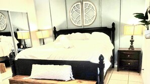 Une chambre à coucher comprenant un lit, des tables de chevet, des lampes, un miroir et un ventilateur de plafond.