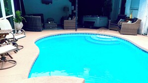 Une piscine dont le bord est revêtu de carrelage, entourée de mobilier d’extérieur et d’un espace abrité avec des sièges.