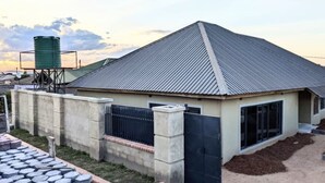 A residential building with a sloped metal roof, a concrete fence, and a water tank in the background. - This 4 bed 3 full bath a big living room, nice kitchen located in Chililabombwe  (Chililabombwe)