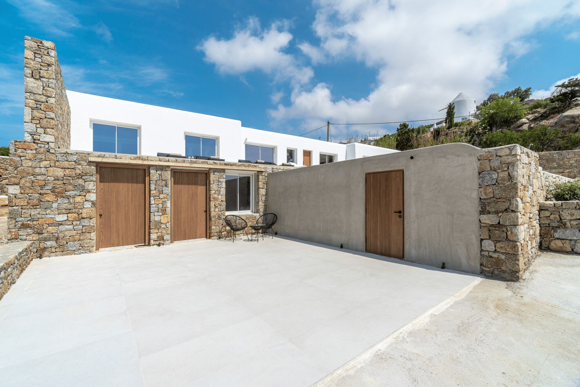 A modern house with stone walls, a concrete patio, and a white building in the background.