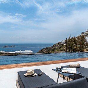 A poolside area with a view of the sea and a rocky hillside. - Elit Villa Psarou Mykonos (Mykonos)