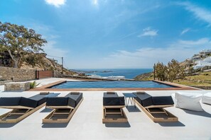 A poolside area with sun loungers and a view of the sea. - Elit Villa Psarou Mykonos (Mykonos)