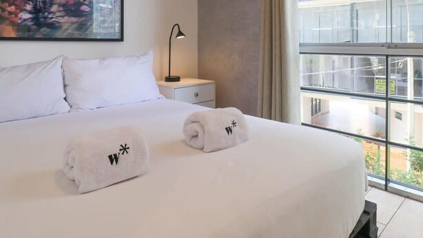 A hotel room with a large bed, a nightstand, a lamp, and a window with a view of buildings. - w Upscale 2BR Near Larcomar Miraflores (Lima)