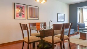 A dining area with a wooden table and chairs, framed artwork on the wall, and a modern pendant light. - w Upscale 2BR Near Larcomar Miraflores (Lima)