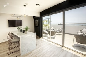 Een moderne keuken met een marmeren eiland, barkrukken en een grote schuifdeur die leidt naar een balkon met zitplaatsen.