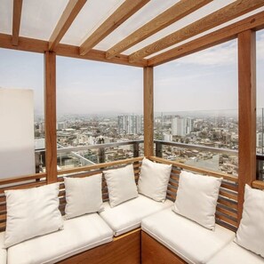 Een balkon met een houten bank en kussens, met uitzicht op de stad.