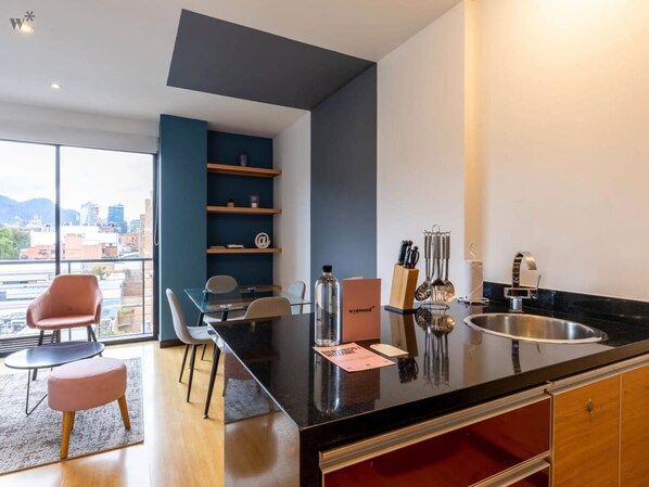 A modern kitchen with a black countertop, a sink, and a dining area with chairs and a table.