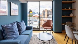 A modern living room with a blue sofa, a round coffee table, and a city view through large windows. - w Vibrant 1BR in Chico (Bogotá)