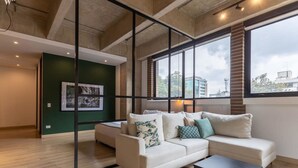 A modern living room with a sectional sofa, a coffee table, and large windows offering a view of buildings and trees. - w Radiant Loft in Parque 93 (Bogotá)