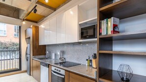 A modern kitchen with white cabinets, a built-in oven, and a microwave. There is a window with a view of a brick building outside. - w Radiant Loft in Parque 93 (Bogotá)