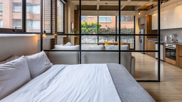 A modern bedroom with a large bed, a view of a balcony, and a kitchen area. - w Radiant Loft in Parque 93 (Bogotá)