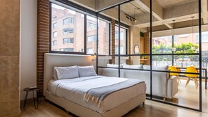 A modern bedroom with a large bed, a small table, and a view of the city through large windows. - w Radiant Loft in Parque 93 (Bogotá)