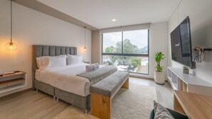 Ein modernes Schlafzimmer mit einem großen Bett, einer Bank, einem Fernseher und einem Fenster mit Blick.
