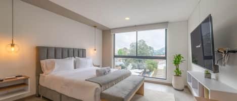 A modern bedroom with a large bed, a bench, a TV, and a window with a view.
