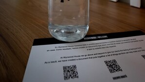 Eine klare Plastikflasche mit dem Aufdruck "POUMAX" auf einer Holzfläche, mit einem QR-Code und Text darunter.
