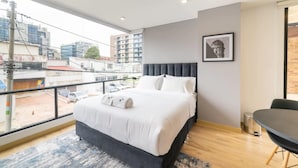 A modern hotel room with a large bed, a view of the city, and a dining area. - w Lovely Loft With Terrace in Santa Ana (Bogotá)