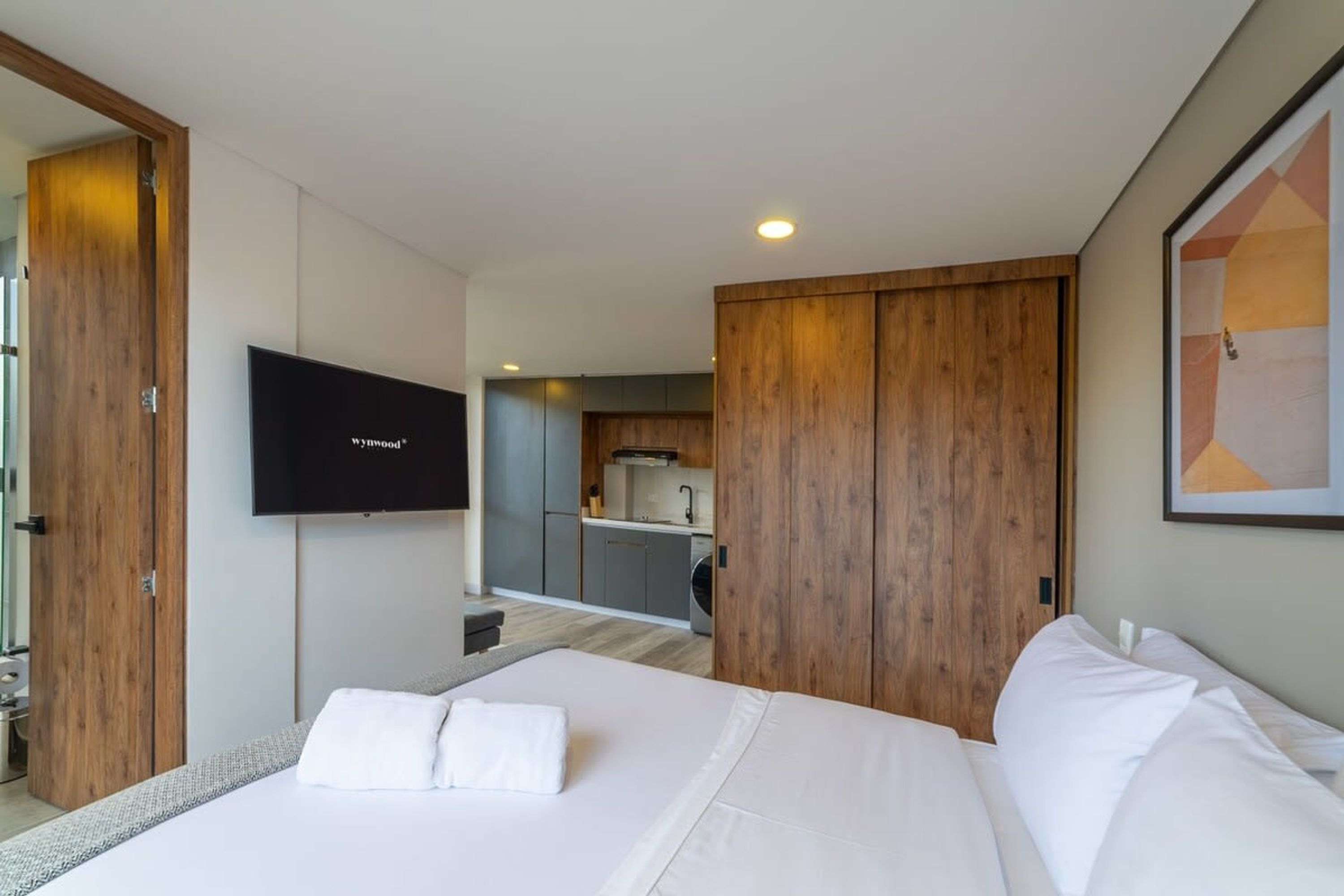 A modern hotel room with a large bed, a TV mounted on the wall, and a wooden wardrobe.