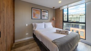 A modern bedroom with a large bed, wooden flooring, and a large window offering a city view. - w Classy Loft in Pasadena (Bogotá)