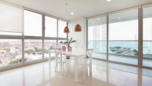 A modern dining area with a white table and chairs, large windows offering a city view, and pendant lights. - w Modern 2BR w AC in Paradisiac Cartagena (Cartagena)