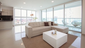 A modern living room with a sectional sofa, a coffee table, and large windows offering a city view. - w Modern 2BR w AC in Paradisiac Cartagena (Cartagena)