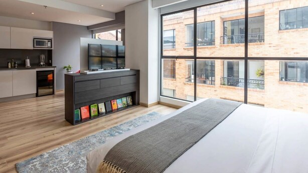 Une chambre moderne dotée d’une grande fenêtre, d’un téléviseur à écran plat, d’une bibliothèque et d’un lit.