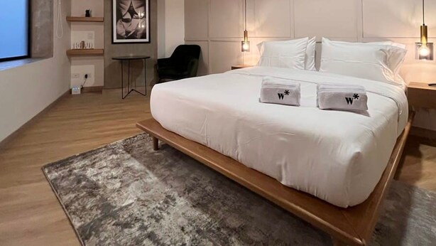 A modern bedroom with a large bed, bedside lamps, a desk, and a chair. - Bright Loft in Laureles (Medellín)