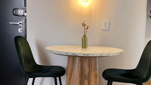 A round dining table with a wooden base, two dark green chairs with gold accents, and a single light bulb on the wall above. - Bright Loft in Laureles (Medellín)