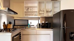 A modern kitchen with white cabinetry, a stainless steel range hood, a black refrigerator, and a microwave. - Bright Loft in Laureles (Medellín)