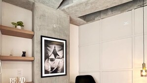 A modern interior with a concrete accent wall, a framed abstract artwork, a black chair, and wooden shelves with decorative items. - Bright Loft in Laureles (Medellín)