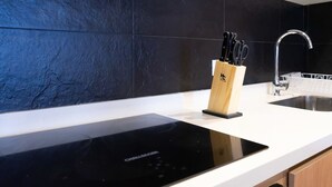 A modern kitchen with a black induction cooktop, a wooden utensil holder, a stainless steel sink, and a dishwasher.