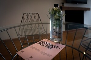 A clear glass bottle with a label on a metal table, a metal chair, and a welcome card. - w Centric 2BR In Cabrera (Bogotá)