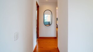 A hallway with wooden flooring, white walls, and a round mirror on the wall.