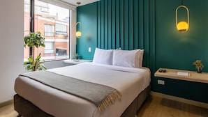 A modern bedroom with a large bed, teal accent walls, and a view of the city. - Amazing 2BR In Centro Internacional (Bogotá)