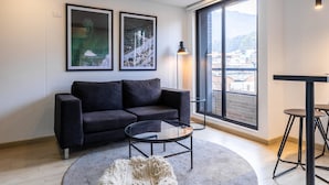 A modern living room with a black sofa, a glass coffee table, and a large window offering a city view. - Amazing 2BR In Centro Internacional (Bogotá)