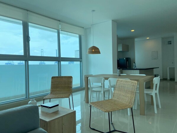 A modern, well-lit room with large windows, a dining area with wicker chairs, and a kitchen in the background. - w Spectacular 3BR w AC in Cartagena (Cartagena)